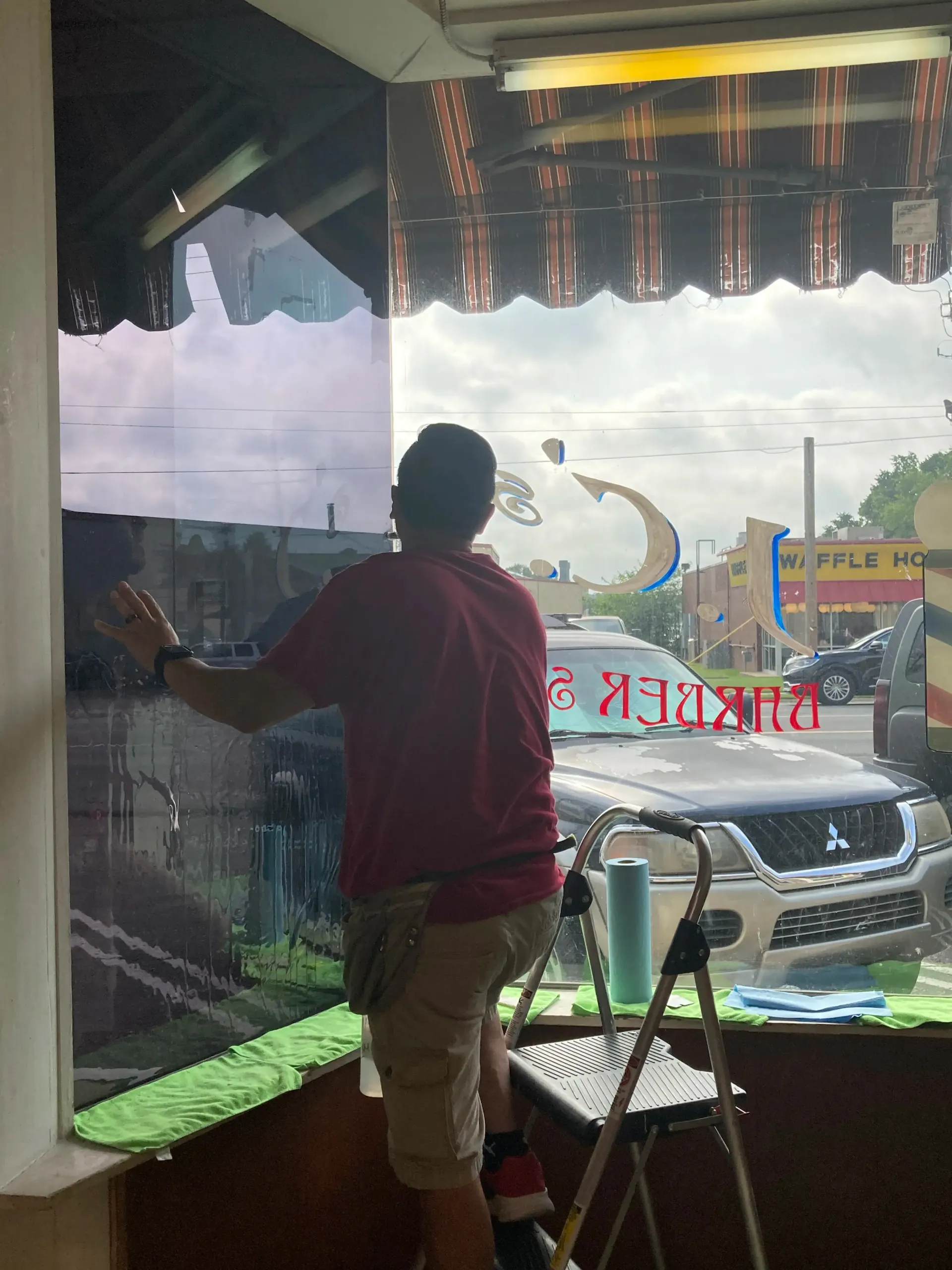 Person installing window film on a storefront window, standing on a step ladder.