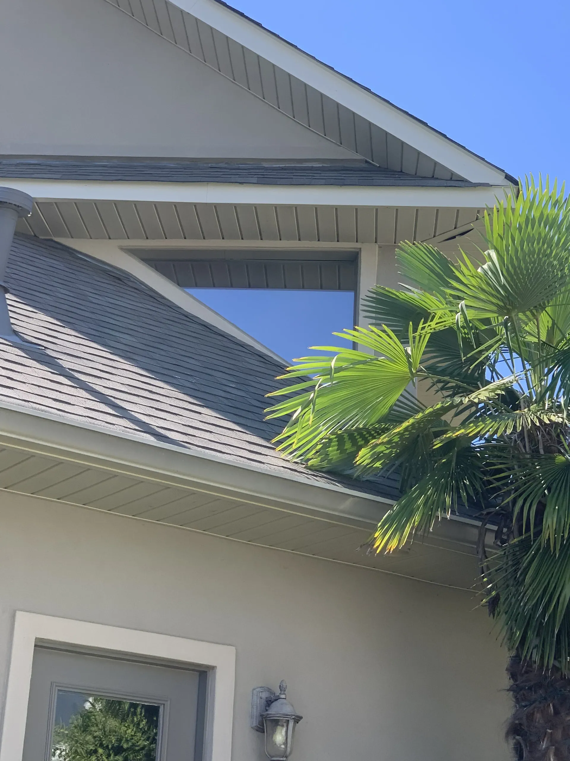 Exterior view of a house with a triangular window under the roof. Palm tree in the right corner.