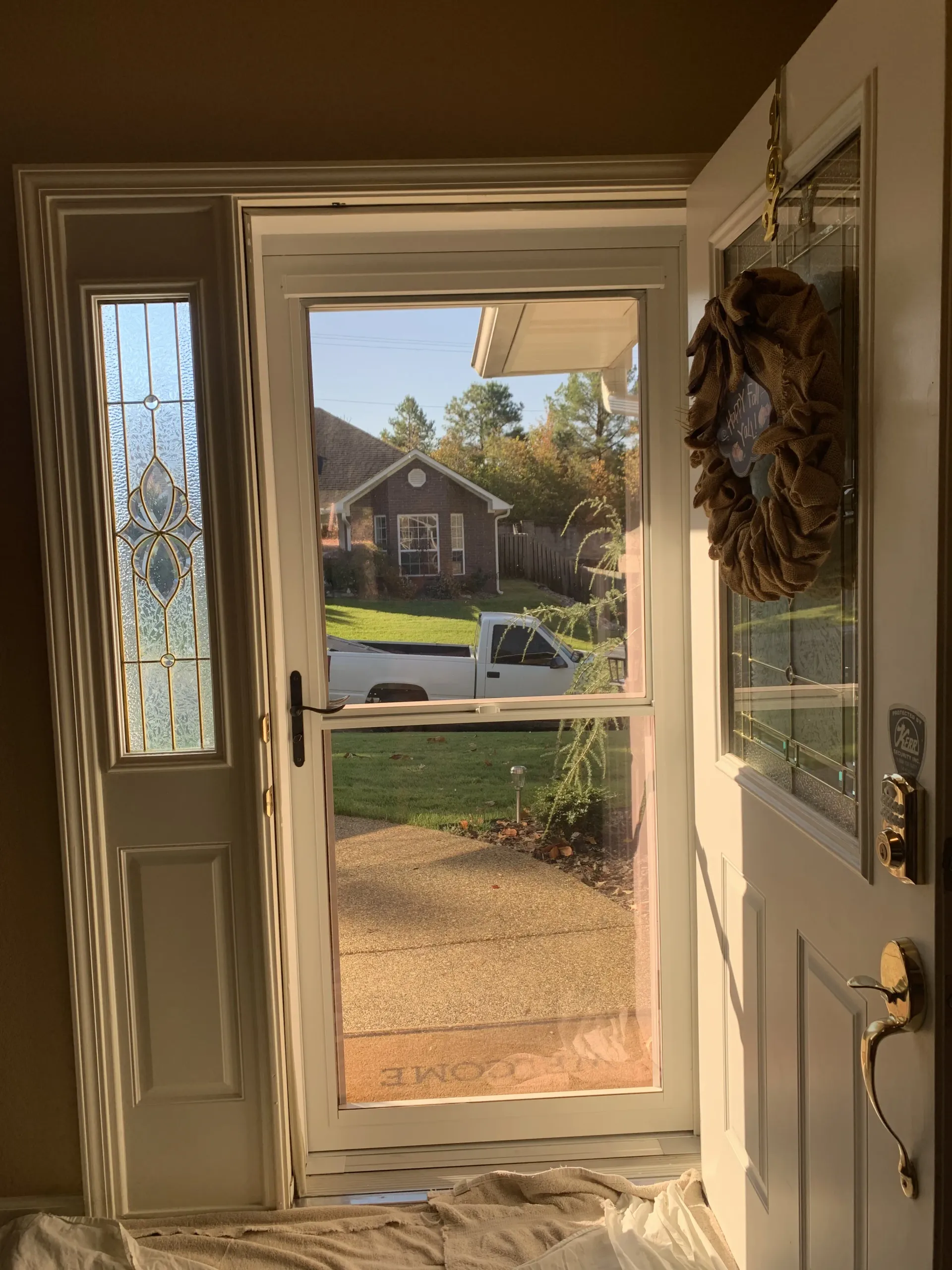 Open white door with screen; view of house, truck, and greenery. Side panel has stained glass.
