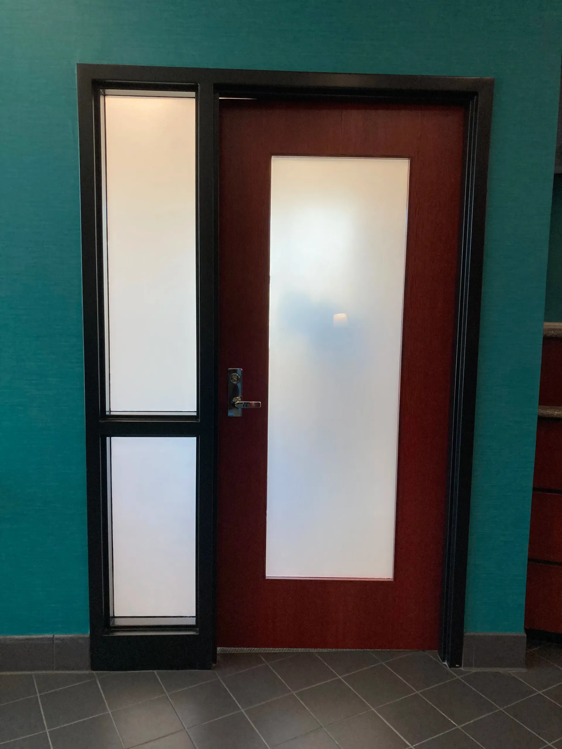 Door with frosted glass panels, next to a tall window; teal wall, dark frame, red door.