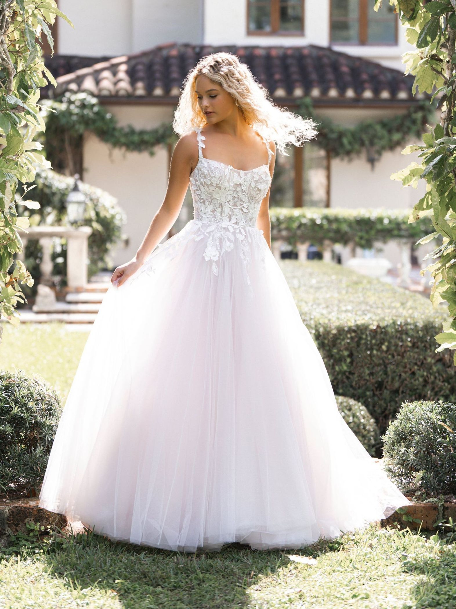 A woman in a white ball gown is standing in the grass in front of a house.