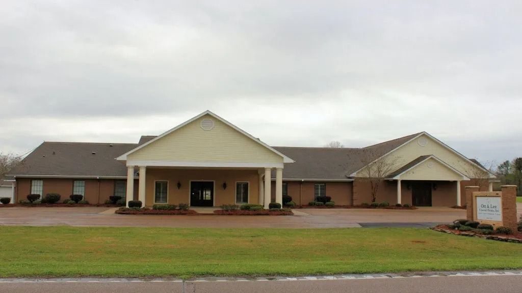 Single-story brick building with tan gabled entrance, front lawn, and sign by the road