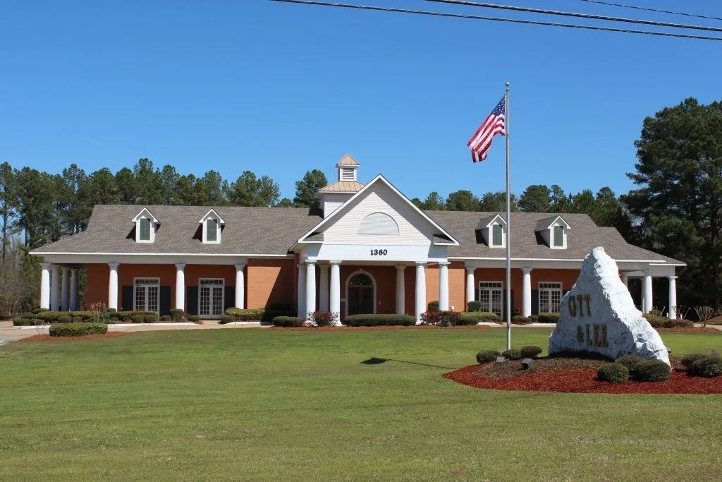 Single-story brick civic building with white columns, American flag, and landscaped lawn under a blue sky