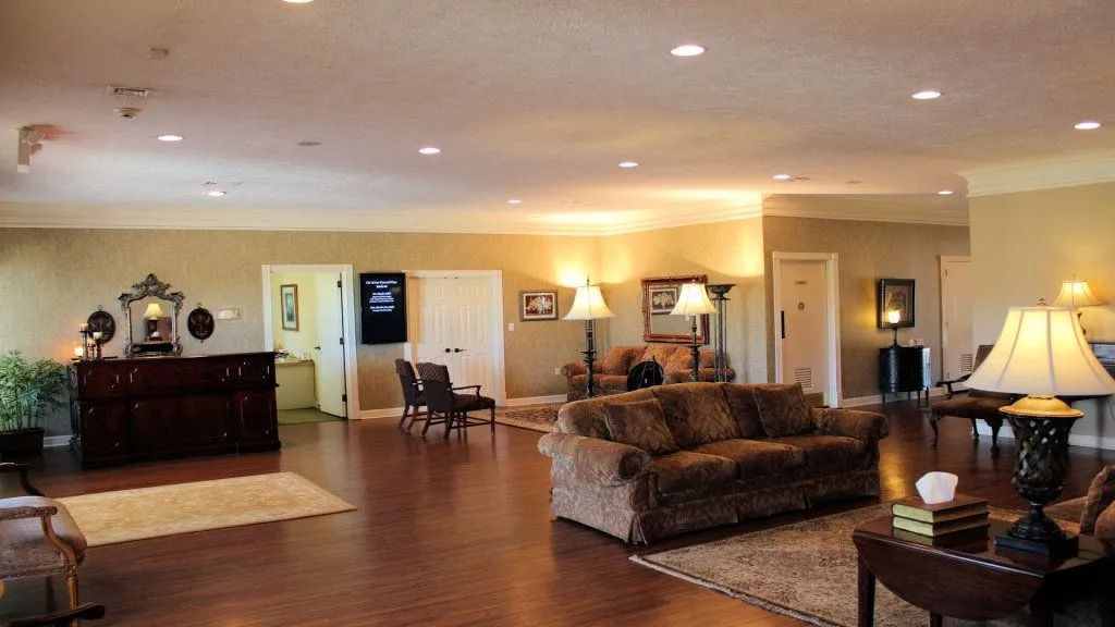 Spacious living room with wood floors, sofas, lamps, and a side table in warm lighting.