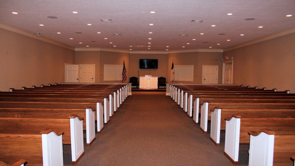 Empty church interior with wooden pews leading to the altar and cross at the front