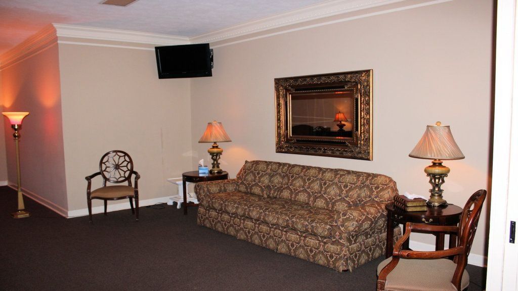 Elegant hotel lounge with patterned sofa, framed mirror, lamps, and chairs against beige walls.