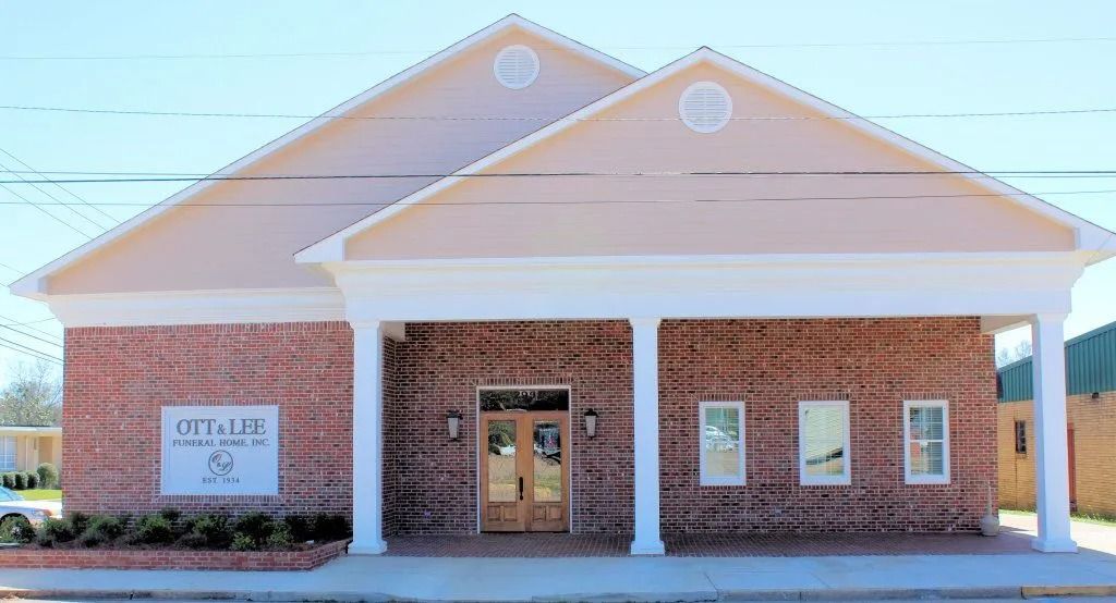 Brick church building with beige roof, white columns, and front entrance under a bright blue sky