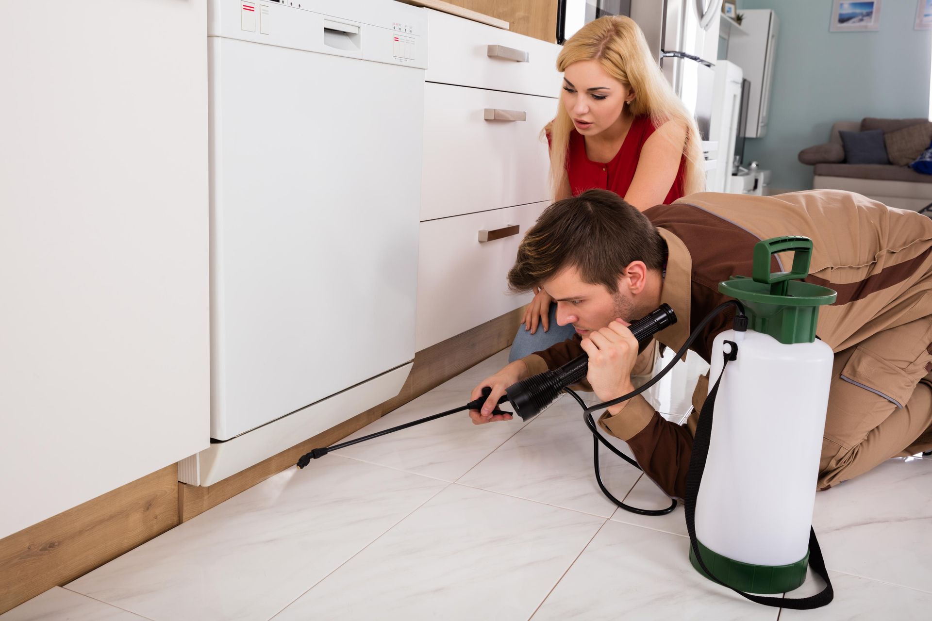A man is crawling on the floor in a kitchen while a woman looks on.
