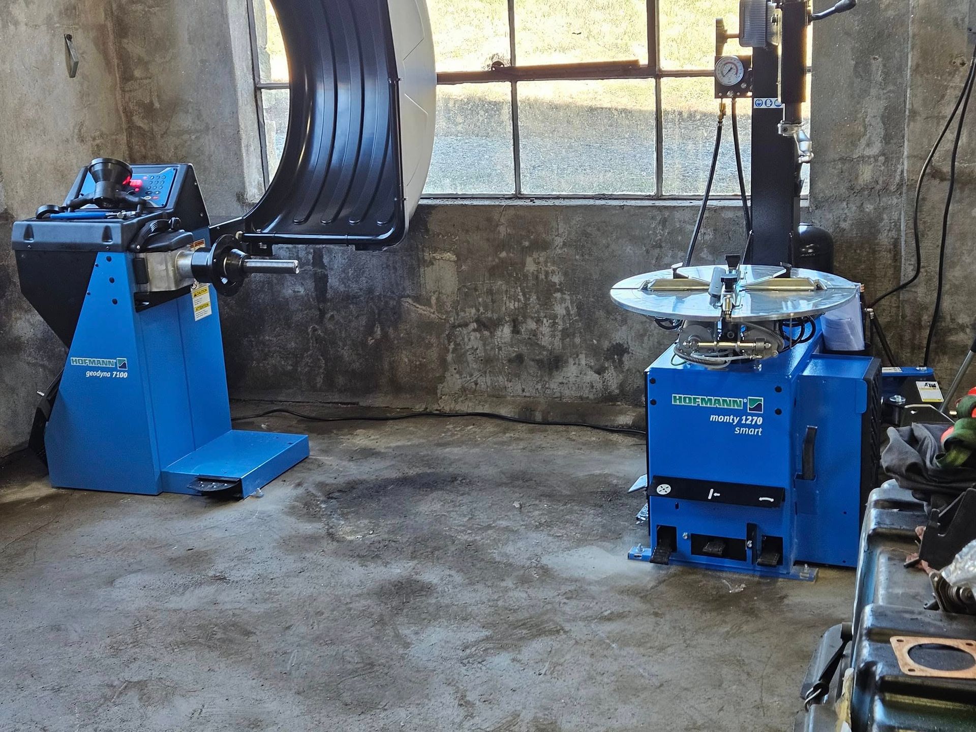 Blue tire-changing machines in a workshop with a tire mounted on one stand.