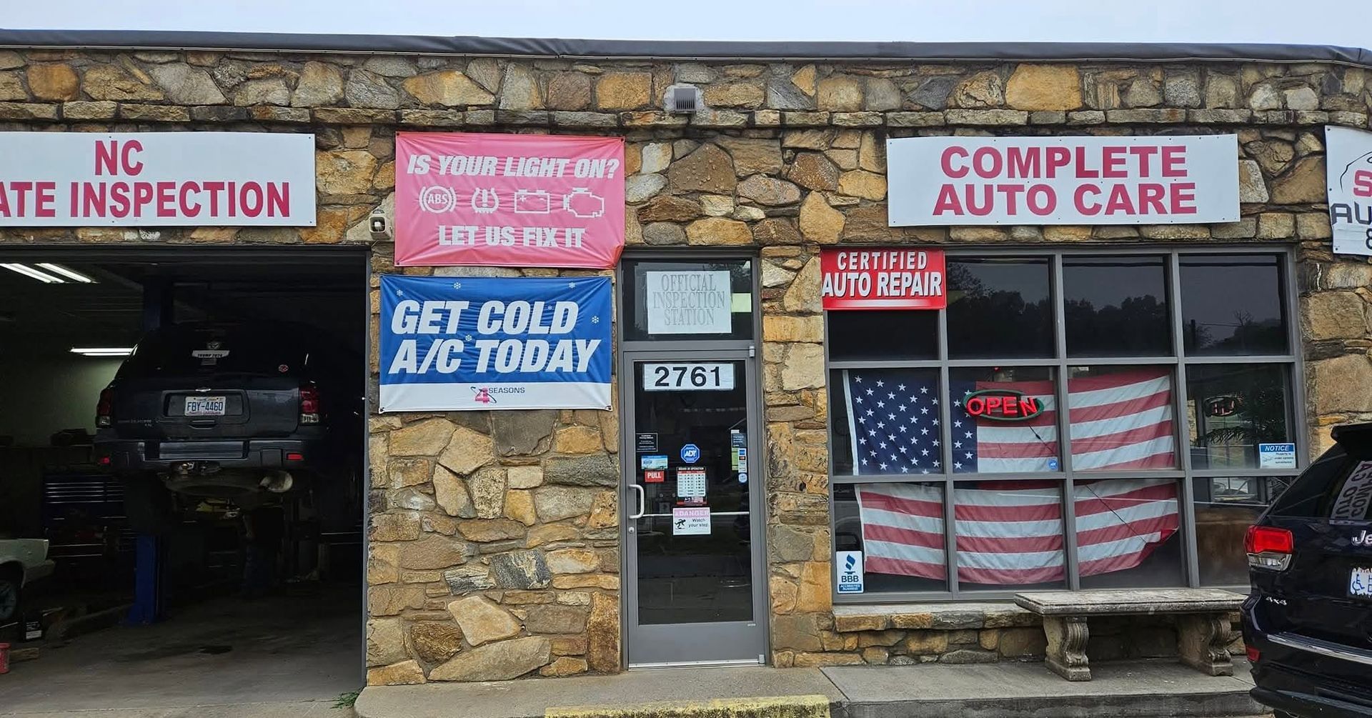 Auto repair shop storefront with stone facade, garage bay, American flag window covering, and inspection signs