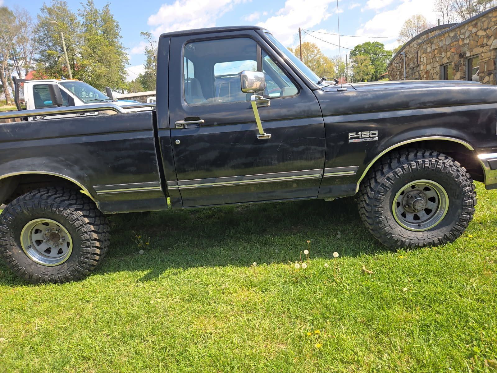 Black lifted pickup truck parked on grass with off-road tires and a light-colored side mirror covering