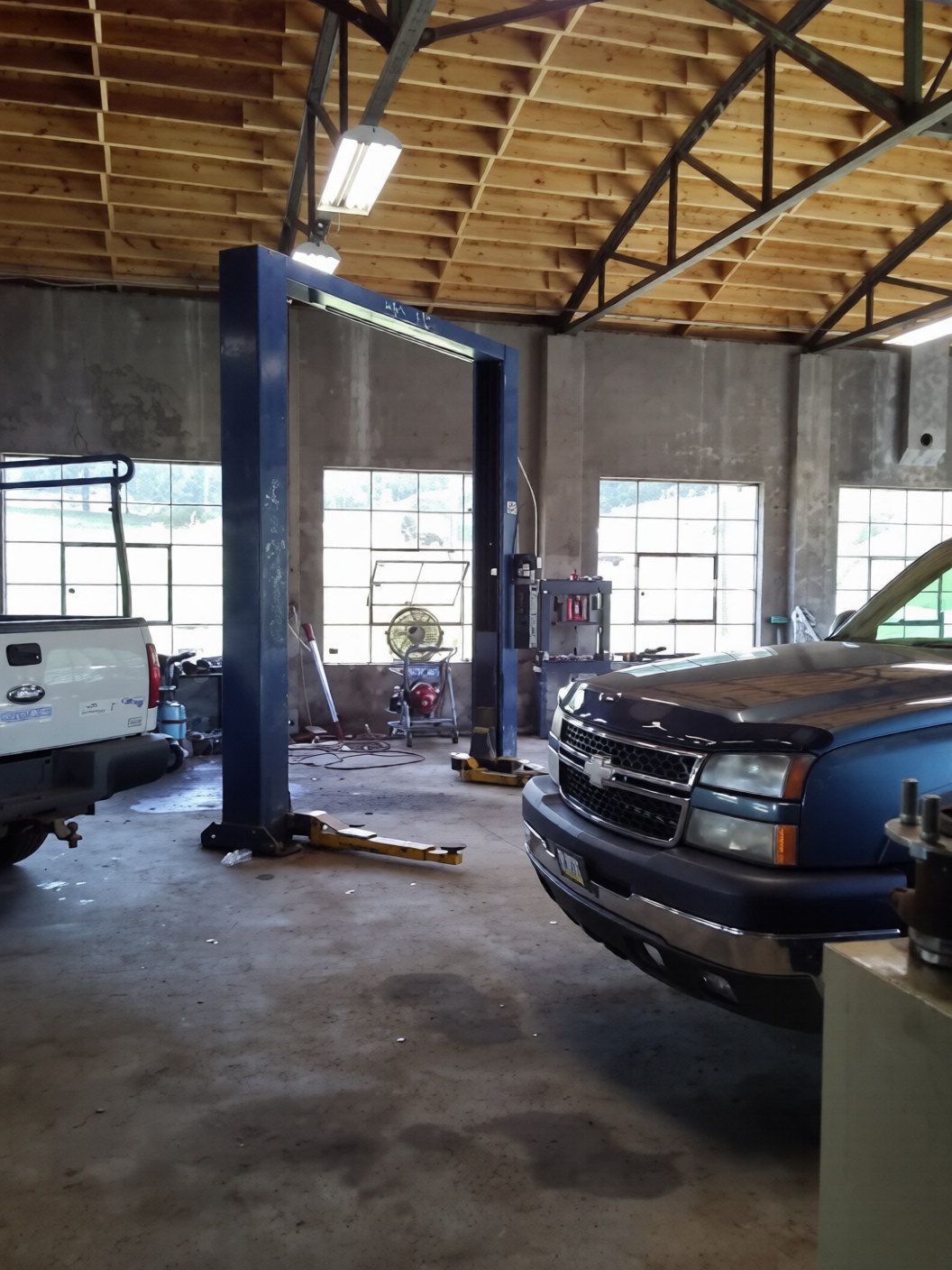 Automotive garage with a truck lift, parked vehicles, and exposed wooden roof beams