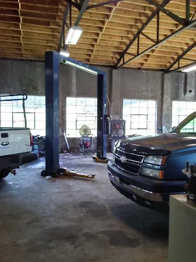 Auto repair garage with a car on a lift and another vehicle parked inside, under a high wooden roof