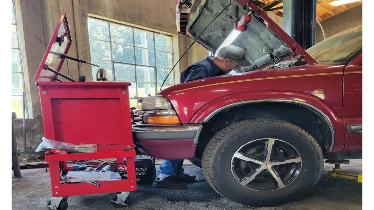 Mechanic under the hood of a red pickup truck beside a red tool cart in a garage