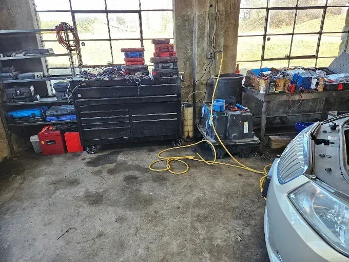 Garage workshop with tool cabinets, equipment, cables, and the front of a silver car by large windows