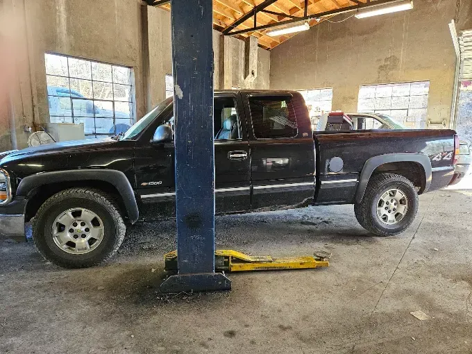 Black pickup truck parked inside an auto repair garage with a lift in front of it