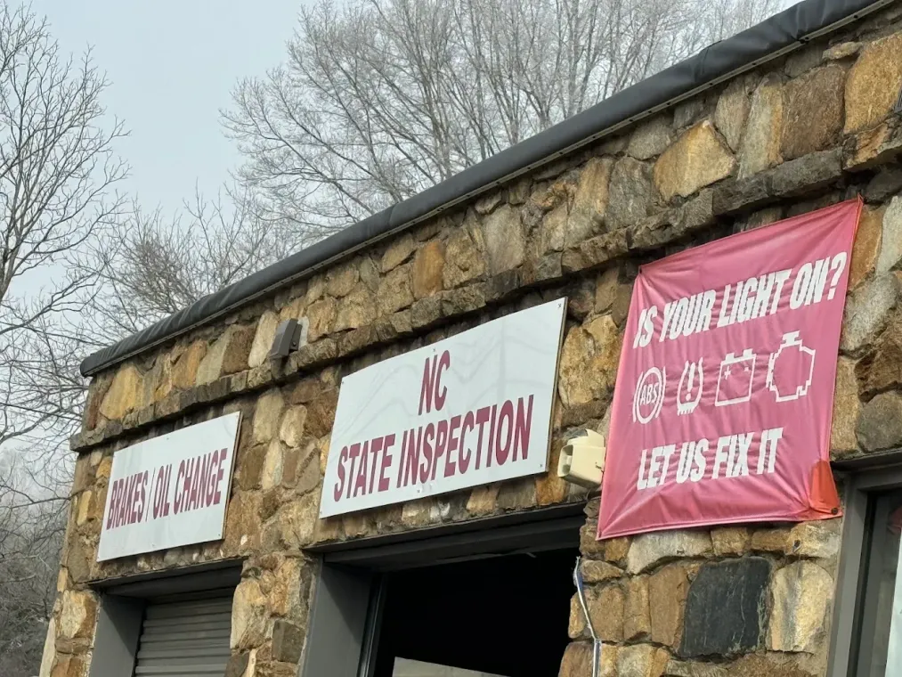 Signage on a stone building: red and white banners for a state inspection station and lost/slash found pet items.