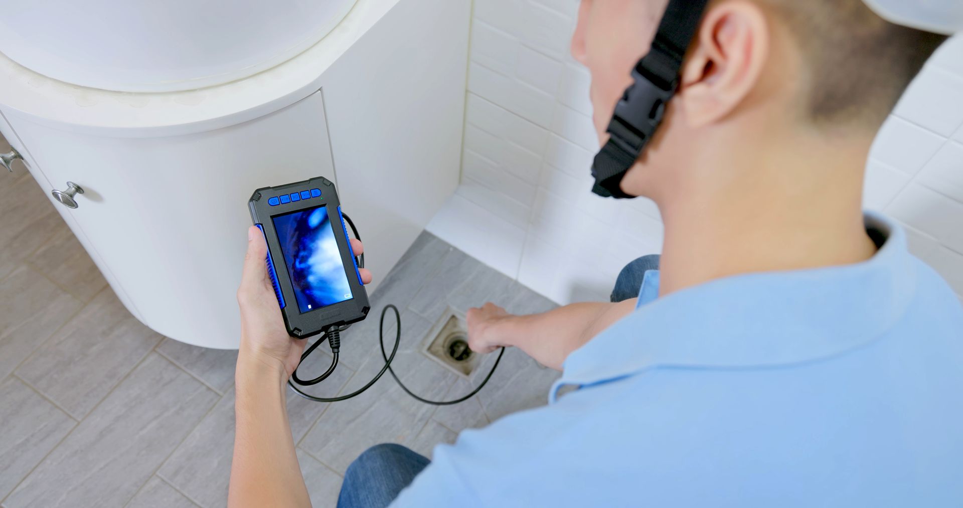 A man wearing a helmet is holding a camera in a bathroom.