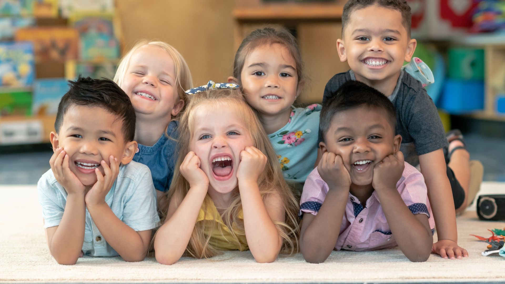 A group of children are laying on the floor and smiling for the camera.