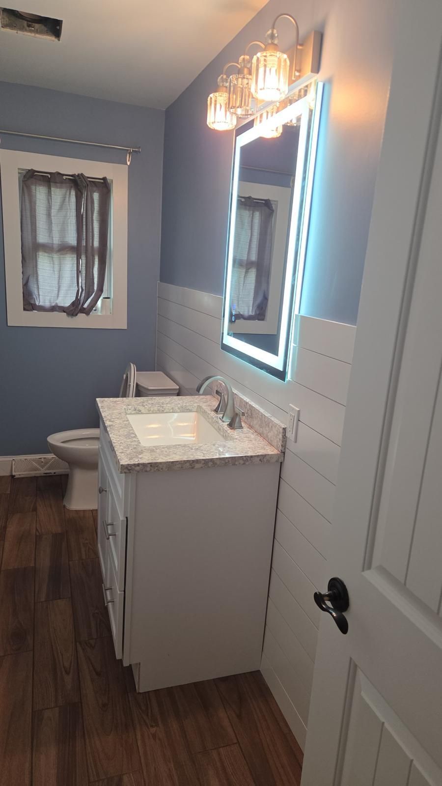 Small bathroom vanity with lit mirror, white sink cabinet, and dark wood flooring.