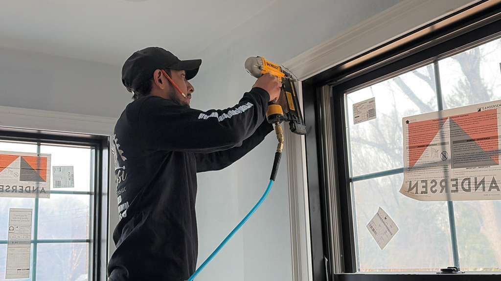 Worker using a nail gun to install trim around a window inside a room