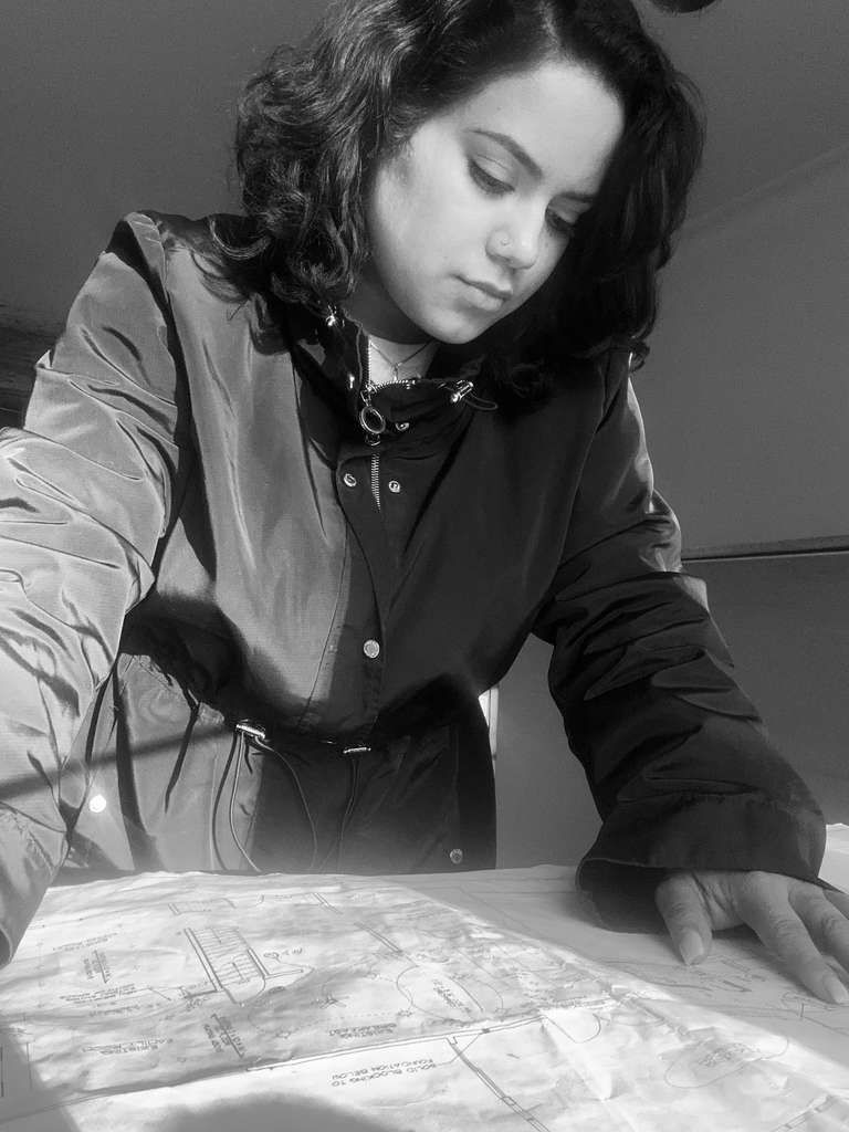 Person leaning over a table, examining a map or blueprint in black and white.