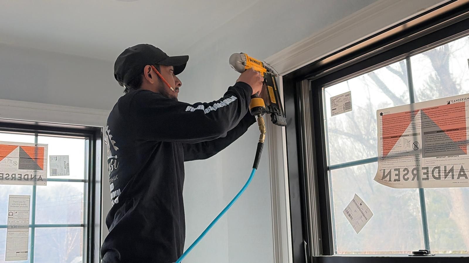 Worker using a yellow drill to install trim around a window inside a room under construction
