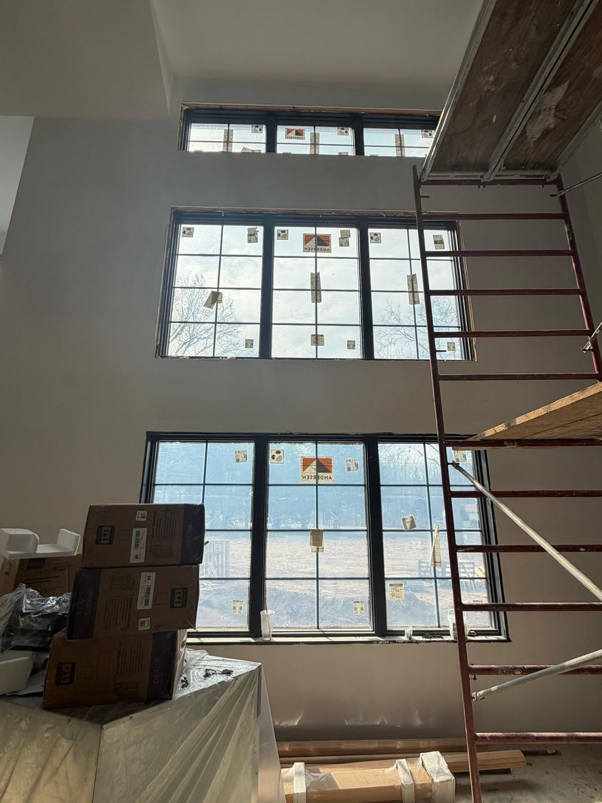 Warehouse interior with stacked boxes, large windows, and a red scaffold beside a white wall