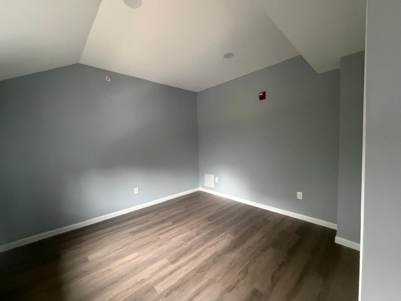 Empty gray room with vaulted ceiling, wood-look floor, and white trim