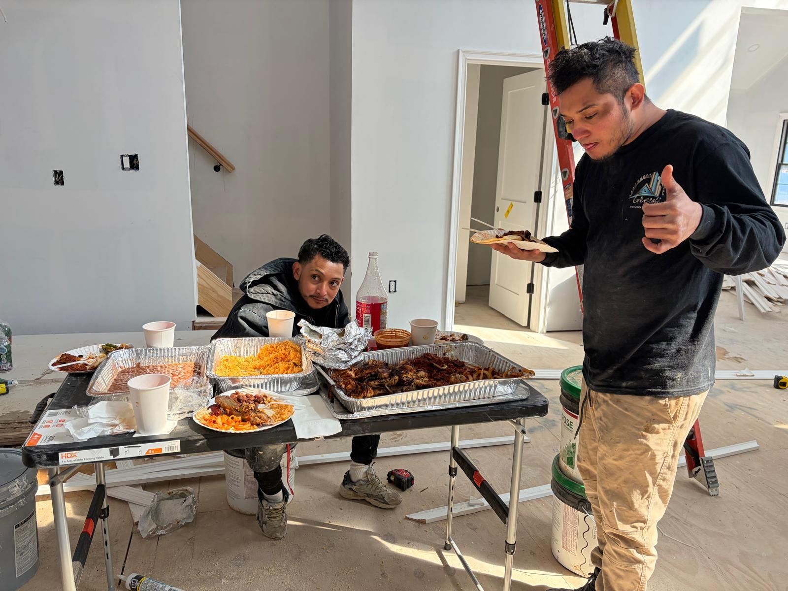Two people at a food table indoors, with trays, cups, and a large roasted meat dish.