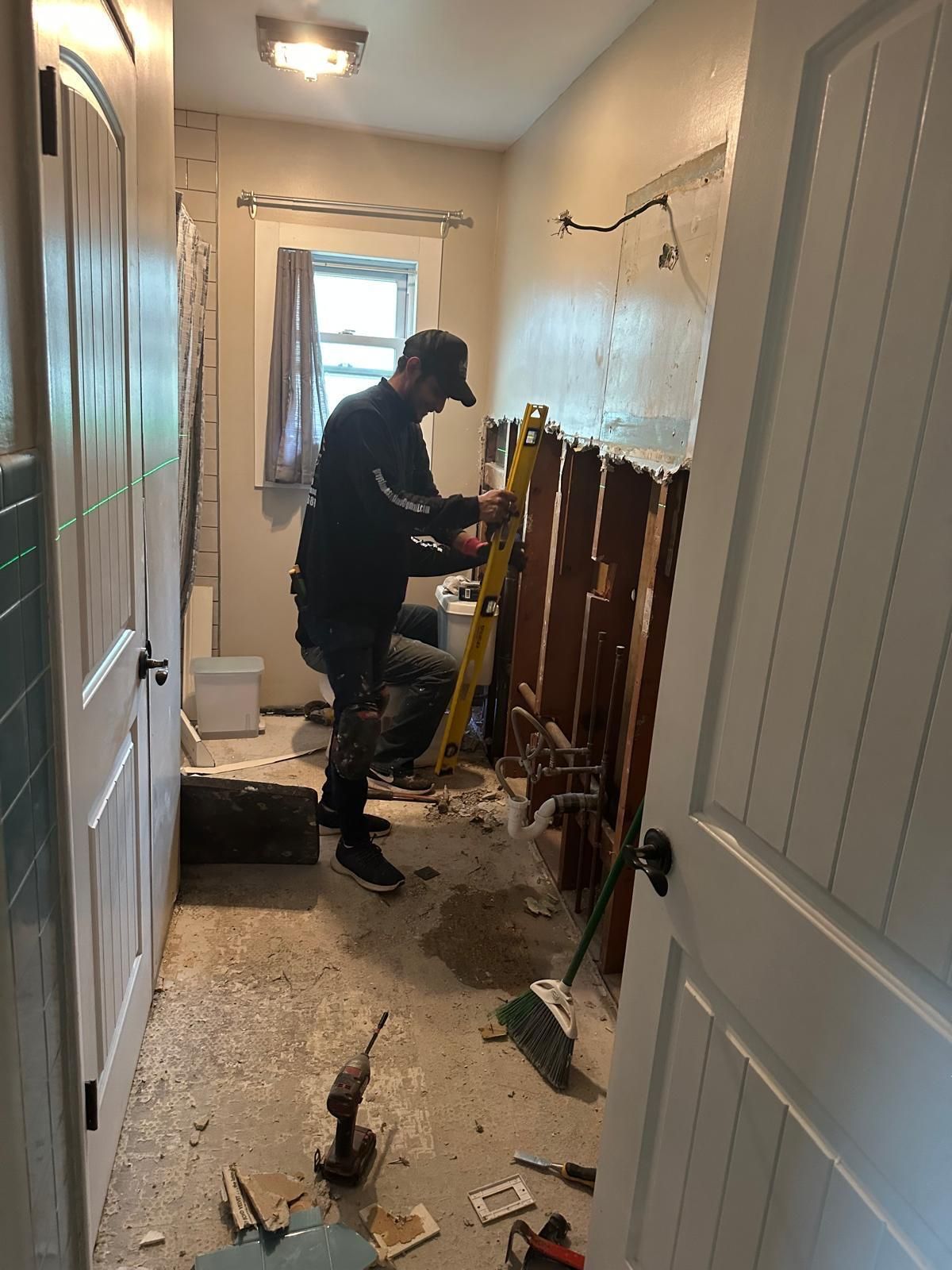 Person demolishing a bathroom wall in a narrow hallway, with debris scattered on the floor.