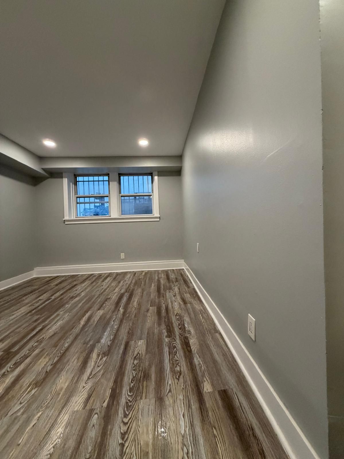 Empty gray room with wood-look flooring and a small window at the far end