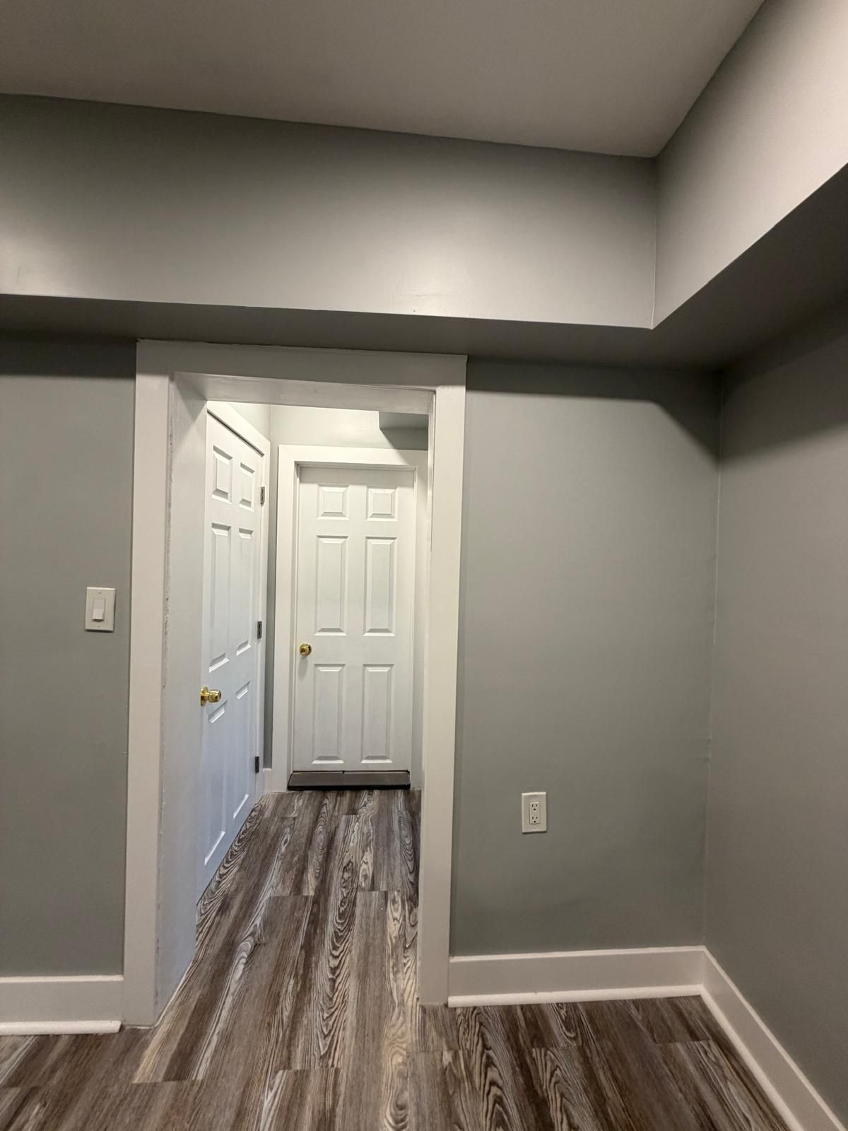 Empty gray hallway with white doors and wood-look flooring, viewed through a doorway