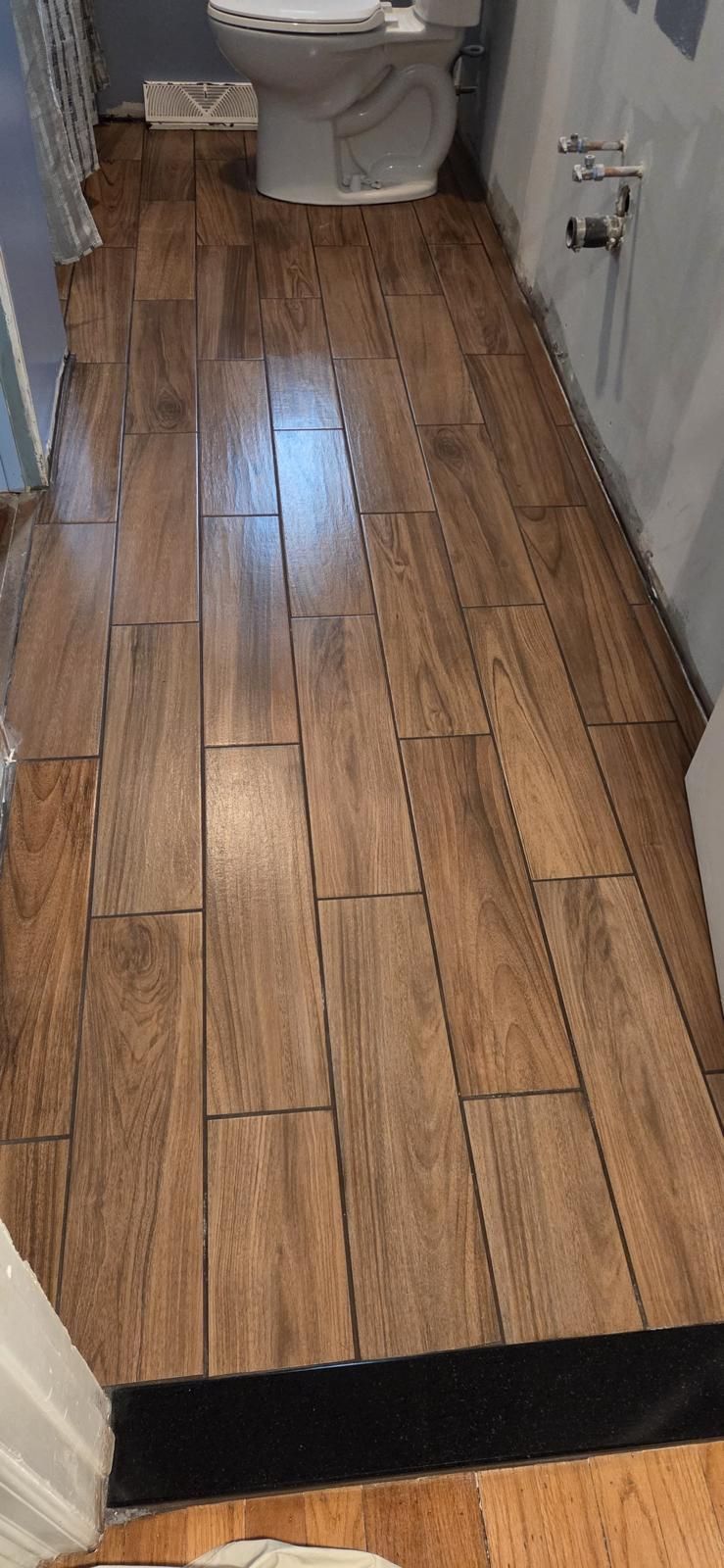 Bathroom with wood-look tile floor, black threshold, and toilet visible at the back.