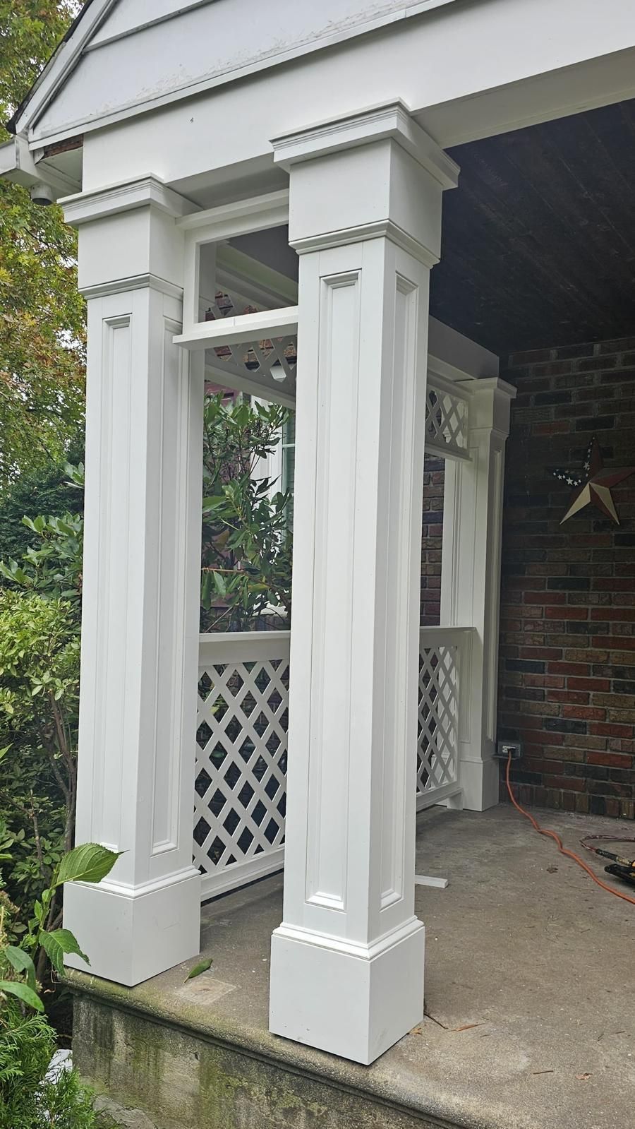 White porch columns with decorative trim supporting an entryway beside a covered patio.