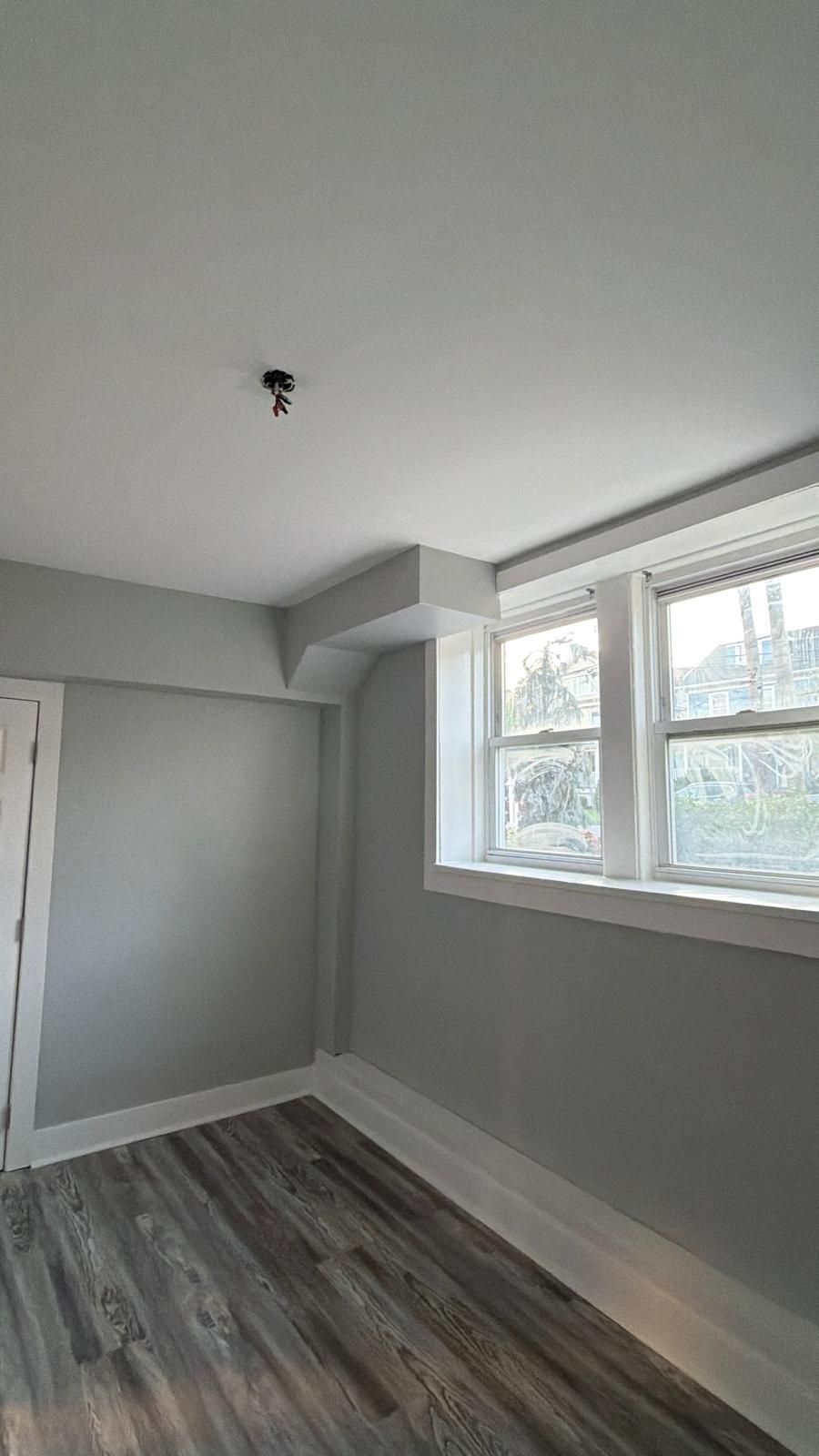 Small empty room with gray walls, wood-look floor, and a large window letting in daylight.