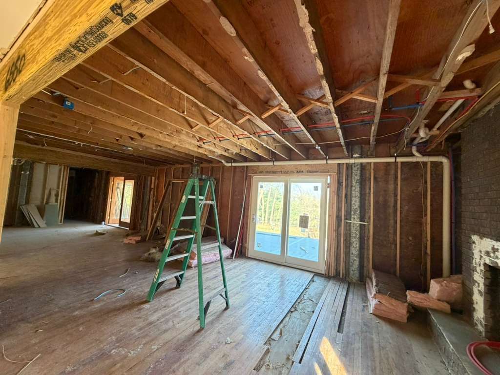 An interior view of a room under renovation with exposed wooden ceiling joists, a green step ladder, and a sliding door.