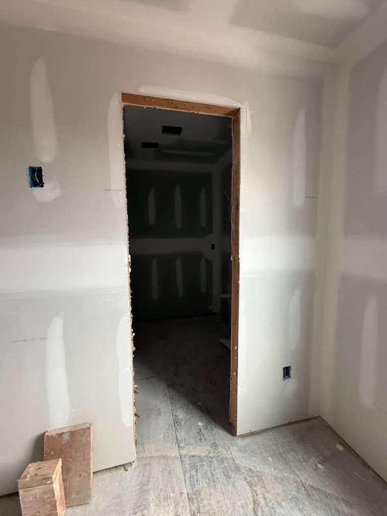 An unfinished room with newly installed drywall, featuring a central doorway leading into a dark, interior space.