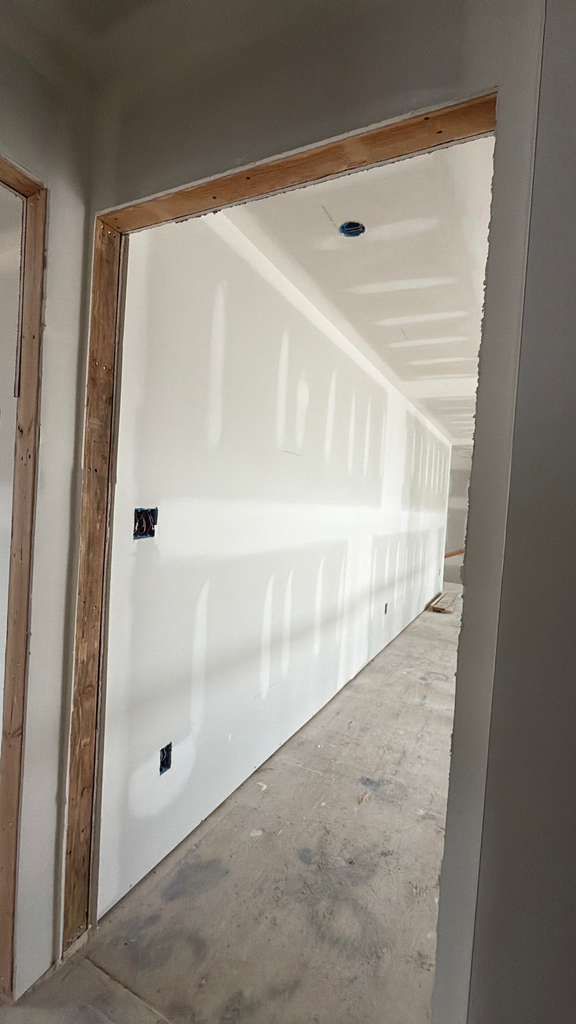 An unfinished room with newly hung drywall, exposed wooden door frames, and a concrete floor under construction.