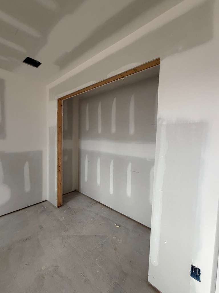 Interior view of a room under construction with white drywall, a recessed closet area, and unfinished wooden trim.