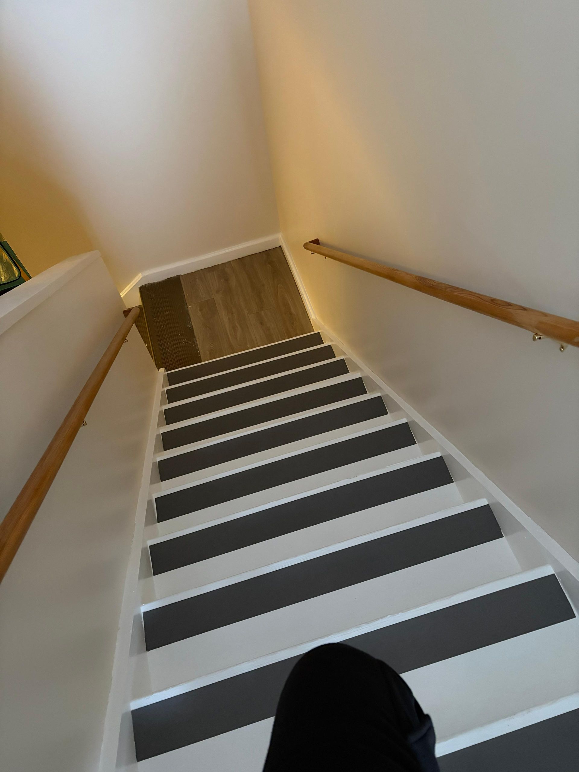 Narrow stairwell with black-and-white striped carpet and wooden handrails, viewed from the top step.