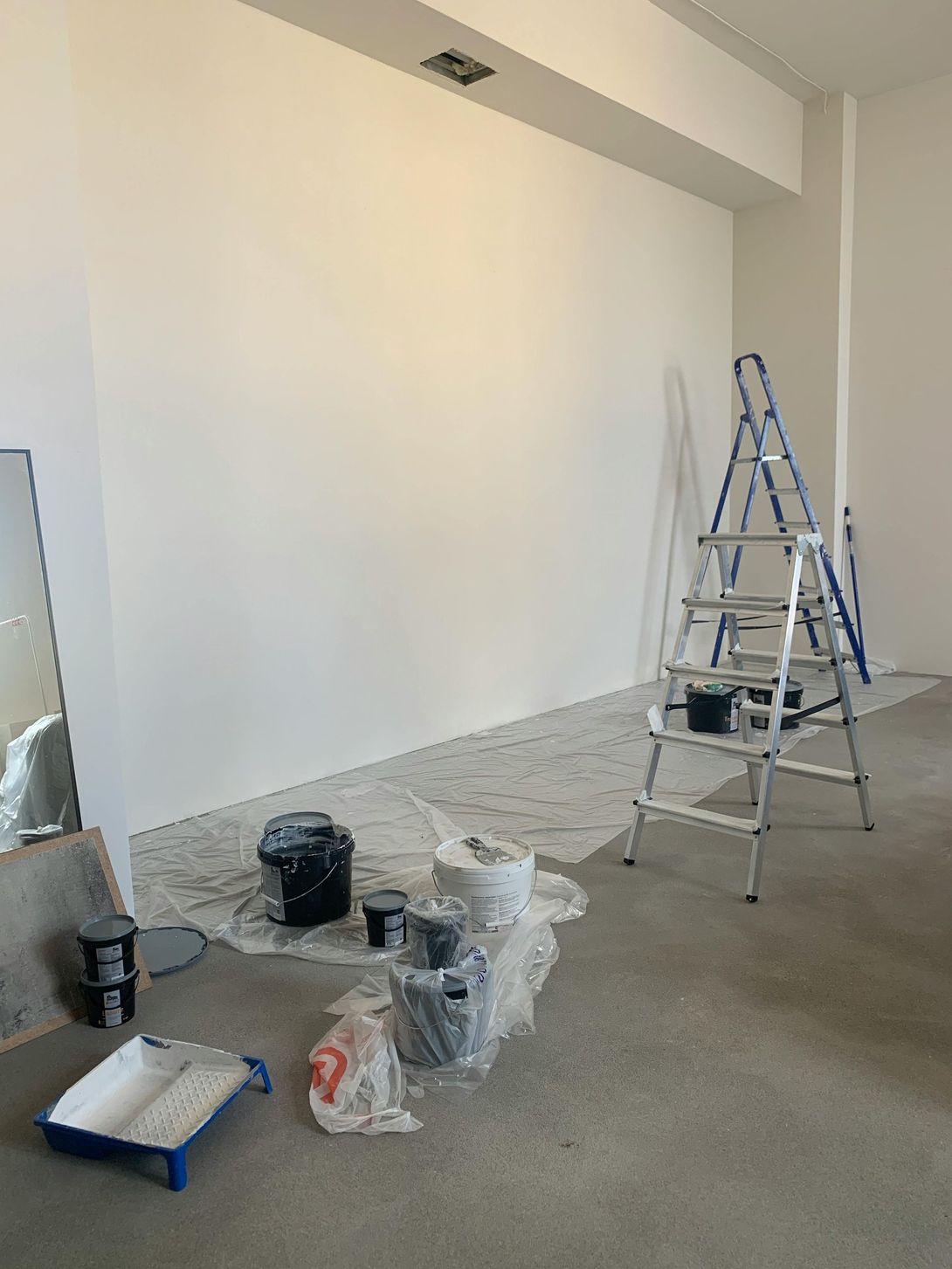 A spacious, empty room with light wood-look floors, tan walls, and an open doorway leading to a windowed area.