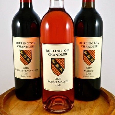 Three bottles of Burlington Chandler wine—a 2018 Cabernet Sauvignon, 2020 Rosé of Malbec, and 2017 Malbec—on a wooden tray.