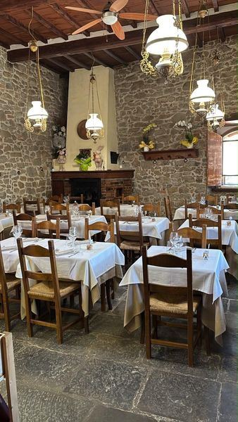 Terrazza esterna del ristorante con tavoli bianchi e sedie rosa accanto a muri in pietra e vegetazione.