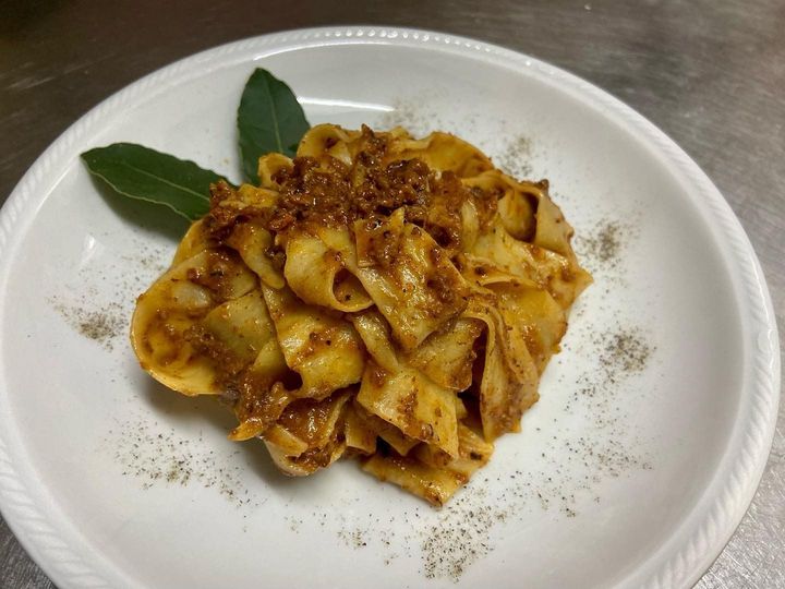 Pasta con gamberi rossi e basilico su un piatto bianco, con un bicchiere di vino bianco sullo sfondo.