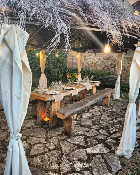 Terrazza esterna del ristorante con tavoli bianchi e sedie rosa accanto a muri in pietra e vegetazione.