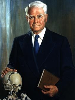 A man in a suit and tie is holding a book and a skull
