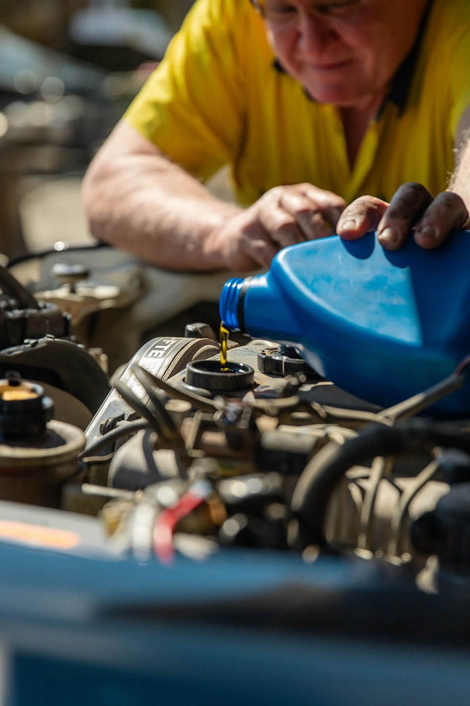 Car servicing in Millmerran Queensland, A man in a yellow shirt is pouring oil into a car engine
