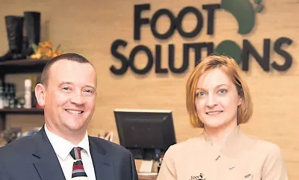 A man and a woman are standing in front of a sign that says foot solutions.