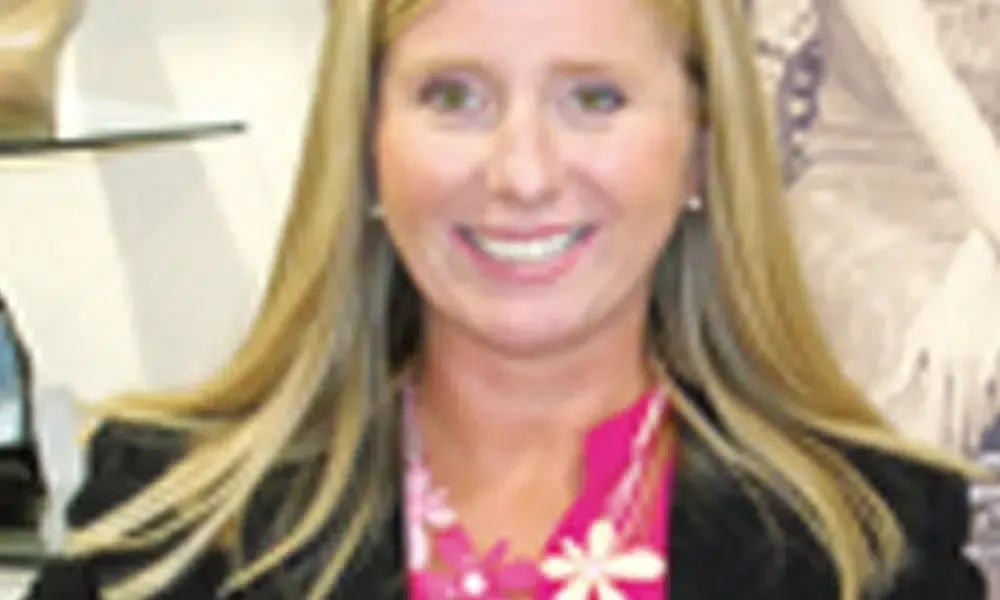 A woman wearing a black jacket and a pink shirt is smiling.